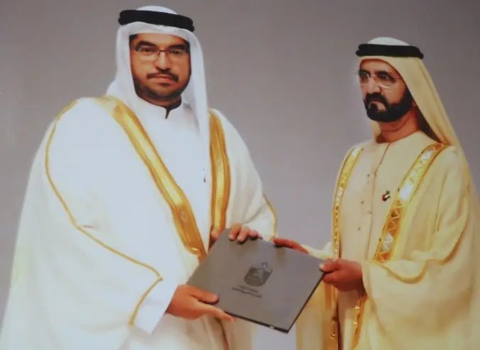 Two men in traditional clothing proudly holding a plaque, showcasing their cultural heritage.