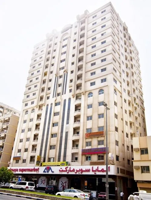 A bustling cityscape with a massive building and numerous cars parked in front, creating a vibrant scene.