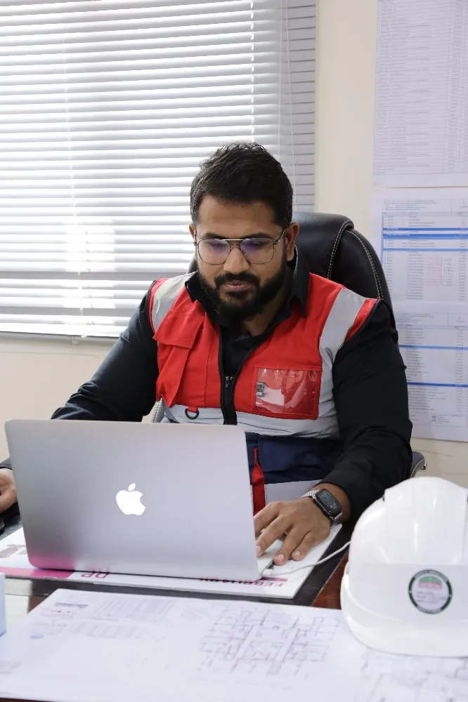 A worker wearing a safety vest working on his laptop