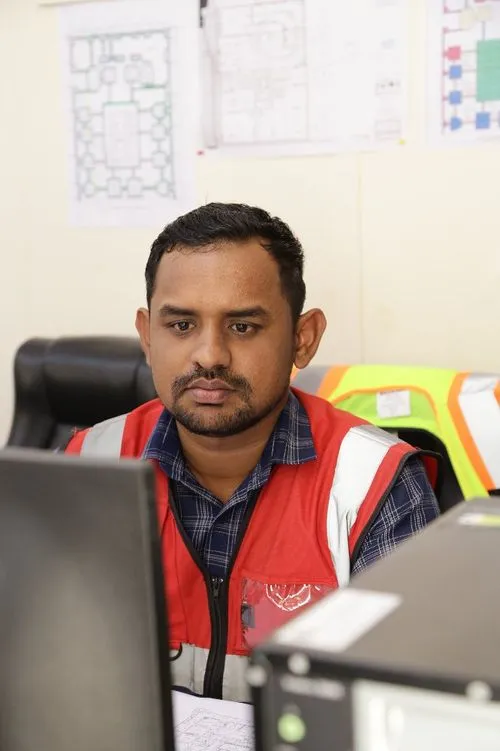 A man in a red vest sitting at a desk with a computer, focused on his work.