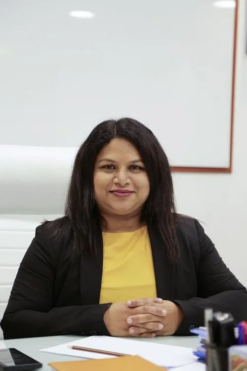 A woman wearing a yellow shirt and a suit, engrossed in her work at a desk.