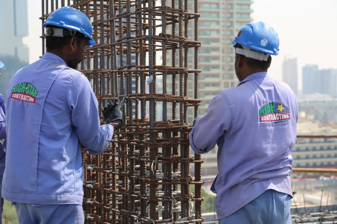 Three men in blue overalls diligently working on a steel structure at a construction site.