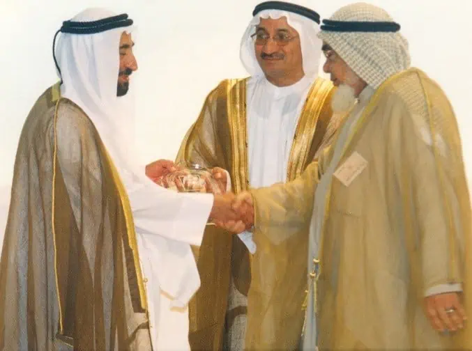 A gesture of friendship and agreement as two men shake hands with a man in a white robe.