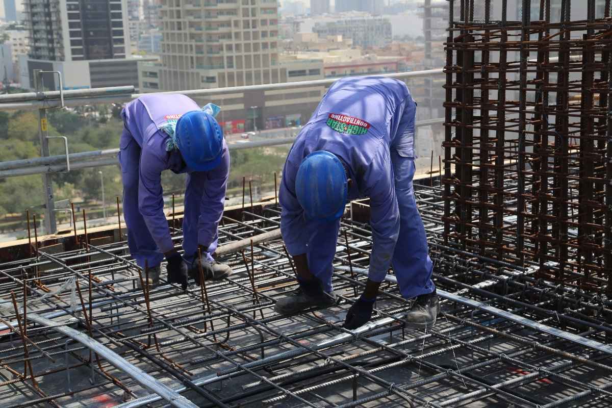 Pair of workers in blue uniforms collaborating on building a steel framework.