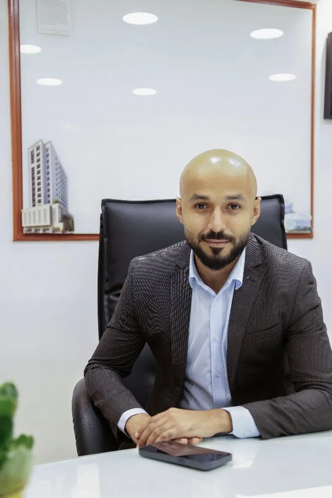 A man in a suit sitting at a desk, looking focused and professional.