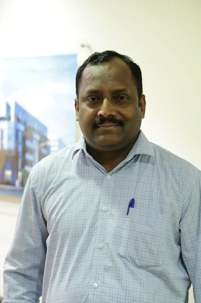 A man in a blue shirt standing in front of a wall.