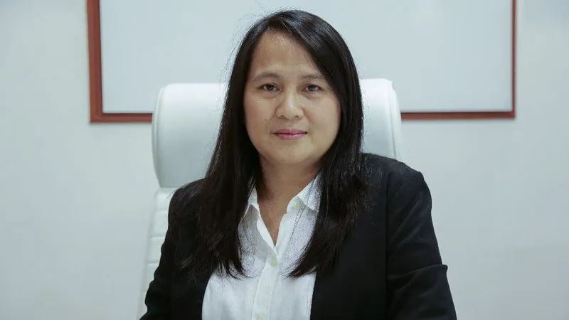 A professional woman in a business suit sitting at a desk, working on a laptop.